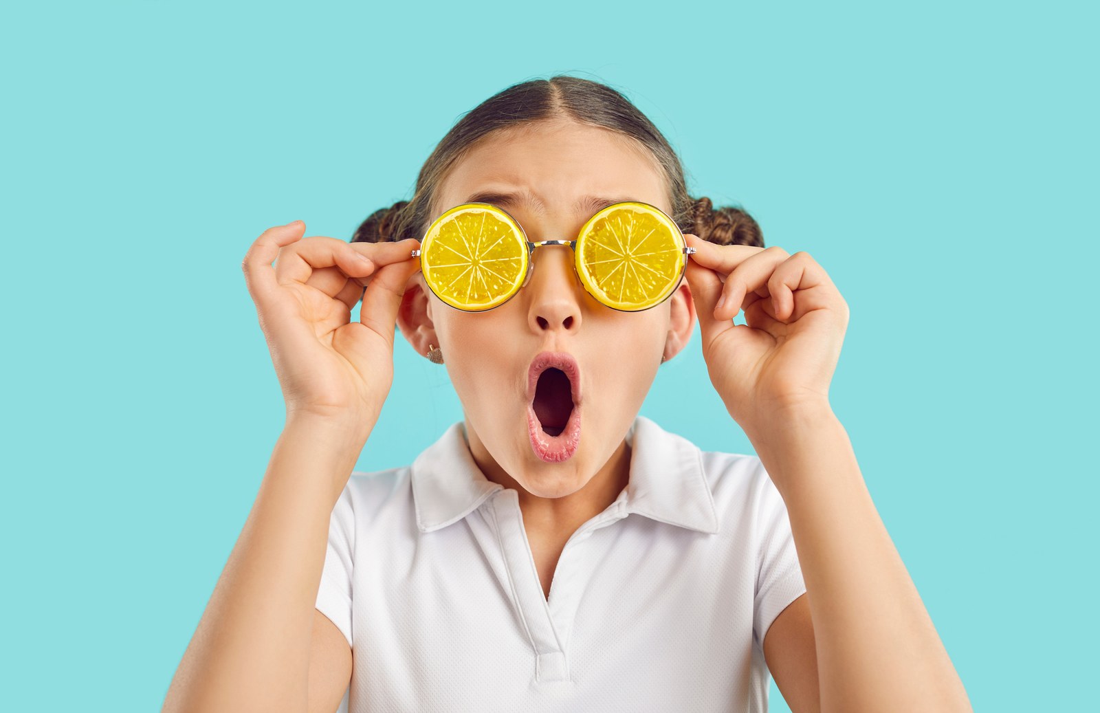 Delighted child holding orange slices over her eyes
